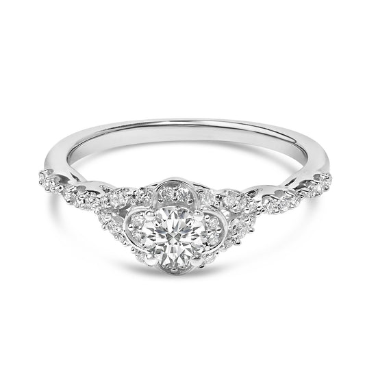 Front angle view of a white metal ring with a central round white gemstone in a four-prong setting, surrounded by smaller round white gemstones in prong settings along the band.