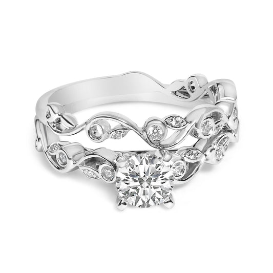Close-up front angle of two white rings, one featuring a large round white gemstone in a prong setting, both with intricate leaf and vine designs accented with smaller round white gemstones in prong settings.