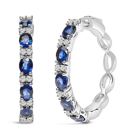 Close-up front and side view of white metal hoop earrings set with alternating oval-shaped blue gemstones and round white gemstones in prong settings.