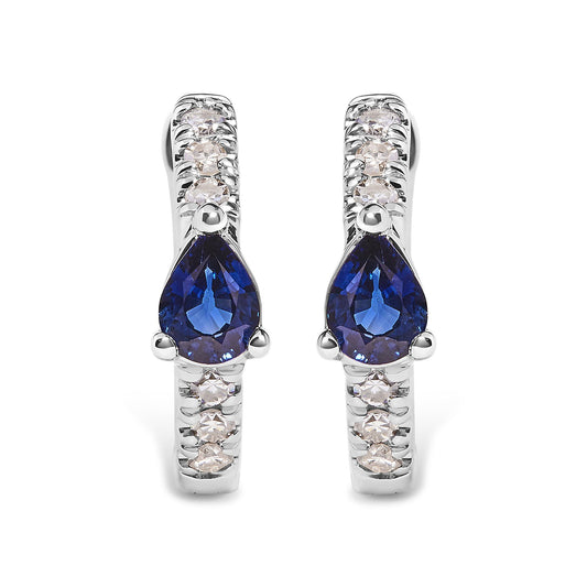 Front-facing close-up of white metal earrings with round white gemstones in pave setting and pear-shaped blue gemstones in three-prong setting.