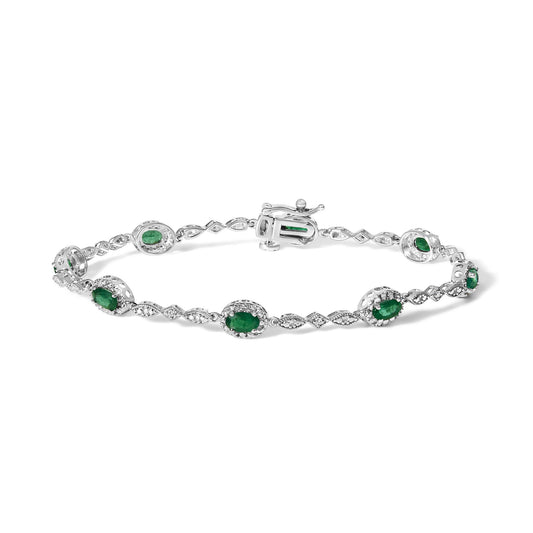 White metal bracelet with alternating oval green gemstones surrounded by white gemstones in pave and prong settings, shown flat in a front angle view.