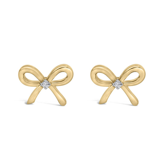 Front view of yellow metal bow-shaped earrings each centered with a round white gemstone in prong setting.