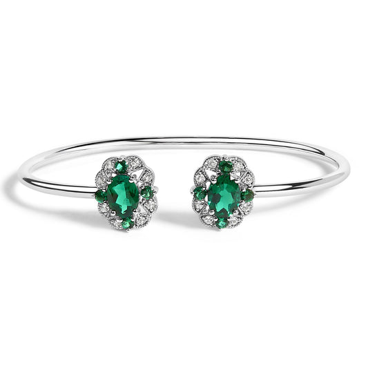 White metal open bangle bracelet with two oval green gemstones surrounded by round green and white gemstones, shown from front angle on a white background.