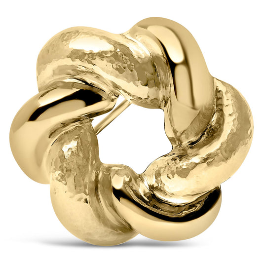 Close-up front angle of a yellow metal brooch with a twisted, chunky, interlocking circular design and a combination of smooth and hammered textures.