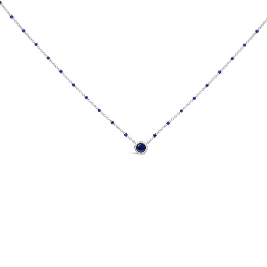 White necklace with a central round blue gemstone in bezel setting and smaller blue gemstones evenly spaced along the chain, shown from a front-facing angle on a white background.