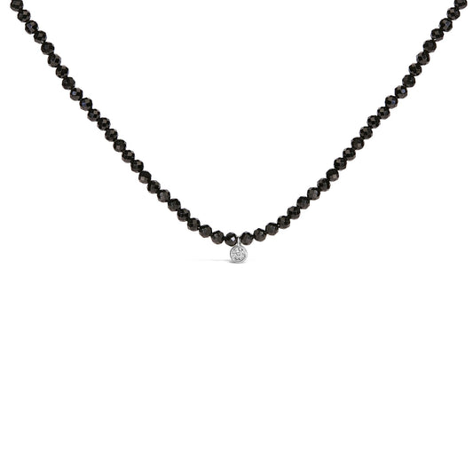 Close-up front view of a white necklace with round black gemstones forming the chain and a single round white gemstone pendant in the center.