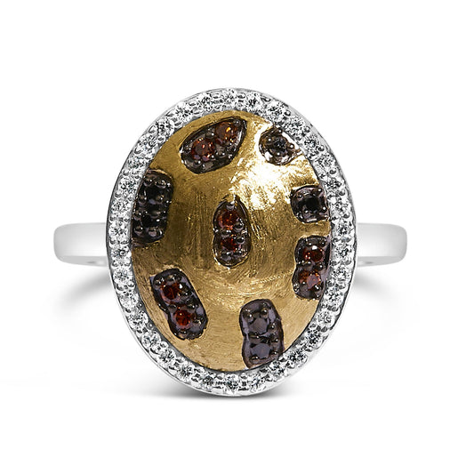 Front-facing shot of a ring with a yellow oval top featuring scattered clusters of red and black gemstones, surrounded by a border of white gemstones on a silver band.
